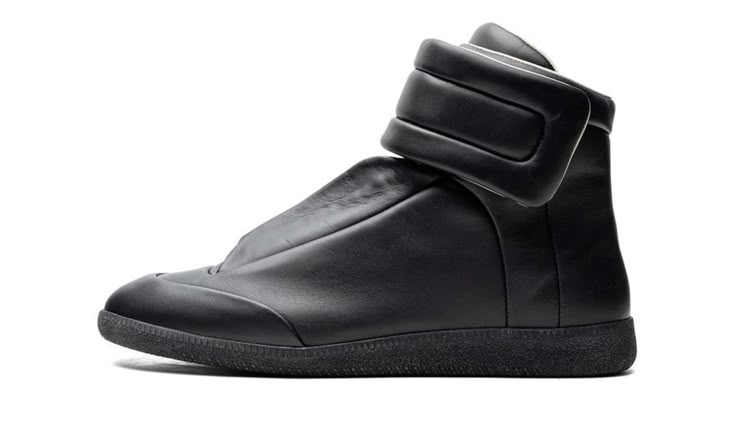 A black high-top sneaker with a unique wrap-around strap design on the ankle, shown in a side profile against a white background.