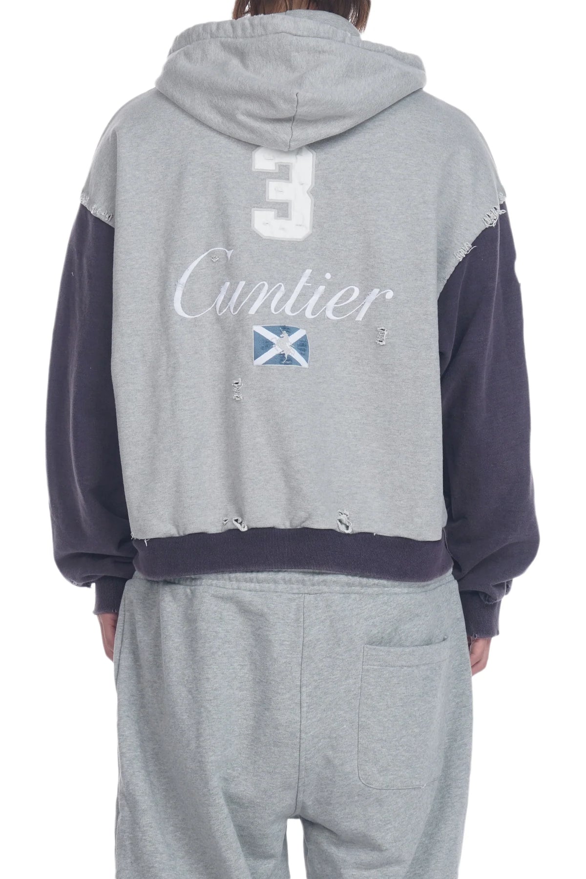 Back view of a person wearing a gray hooded sweatshirt with dark navy sleeves and a distressed hem, featuring the number 3, 'Cuntier' script, and a Scottish flag graphic on the back, paired with matching gray sweatpants.
