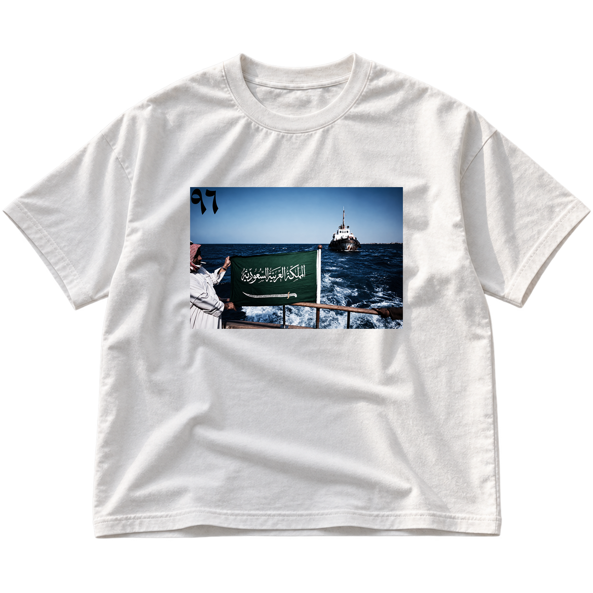 A white short-sleeve crewneck t-shirt with a rectangular graphic print on the front showing a person holding a Saudi Arabian flag on a boat.