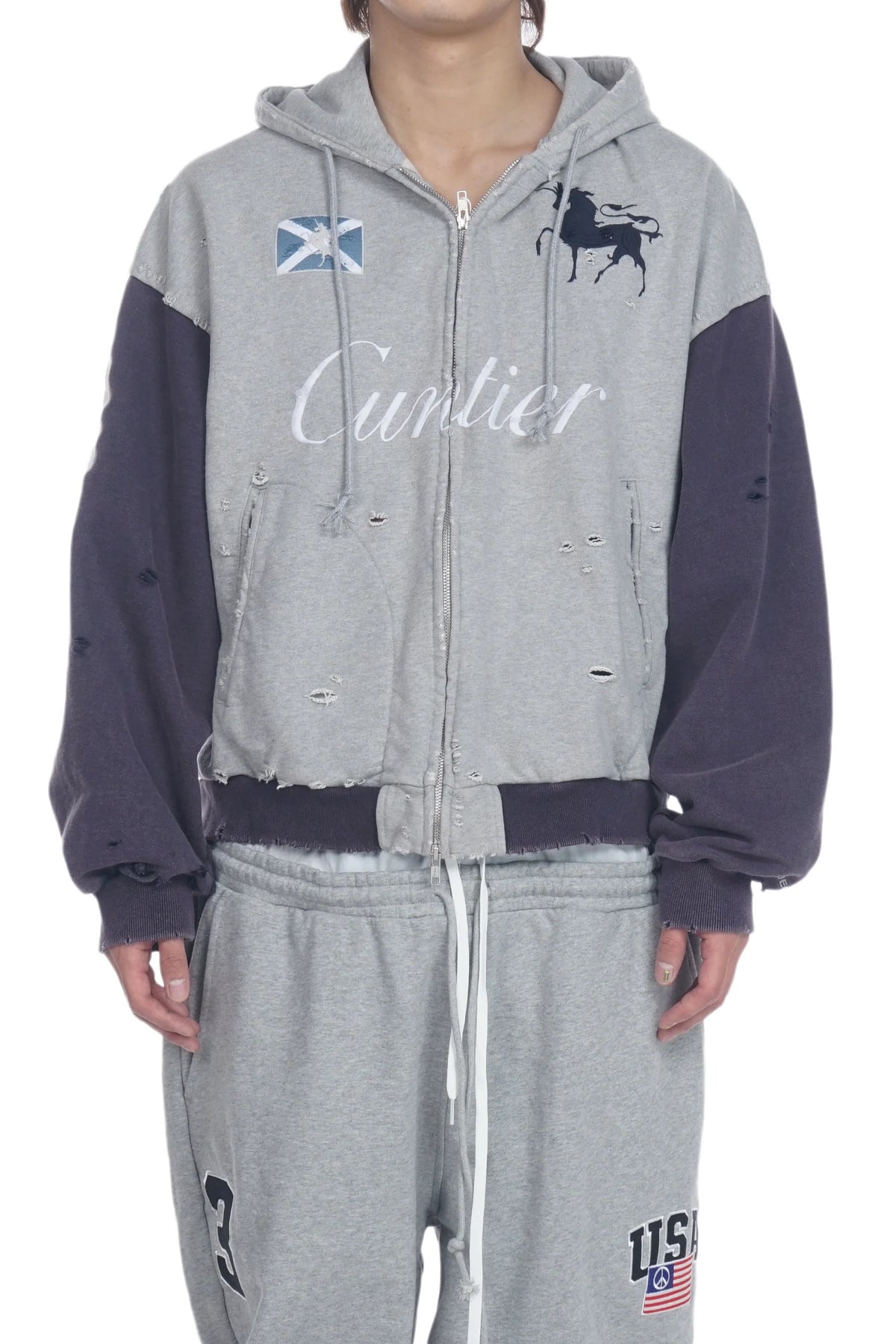 A person wearing a distressed zip-up hoodie and matching sweatpants. The hoodie is heather gray with dark navy sleeves and hood, featuring a white 'Curlier' script across the chest, a Scottish flag patch, and a horse graphic.