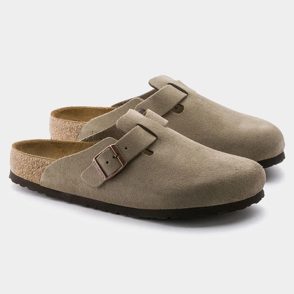 Pair of beige suede clogs with a buckle on a light gray background