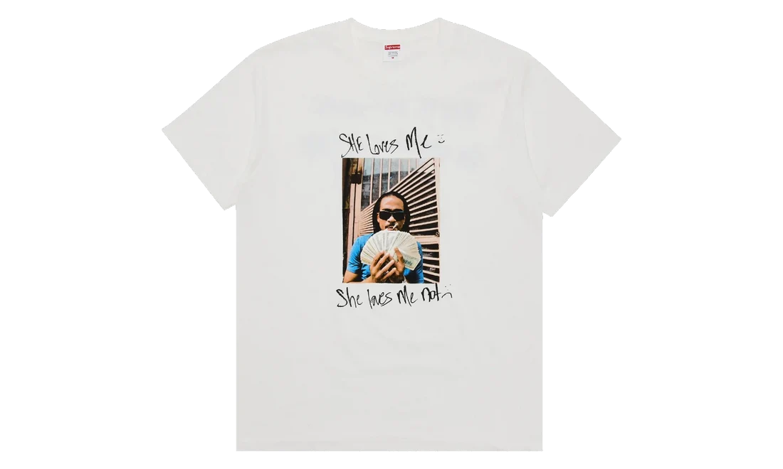 A white short-sleeve crewneck t-shirt featuring a graphic print on the front. The print includes a central rectangular photo of a person holding a fan, with the handwritten text 'She loves me' above and 'She hates me' below.